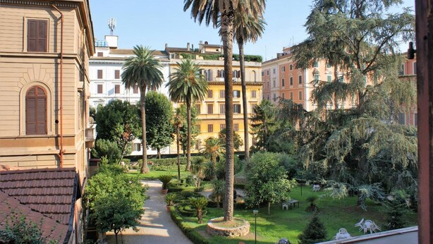 A courtyard with a pathway, palm trees, and buildings with classic architecture. - Capitolium Rooms (Rome)