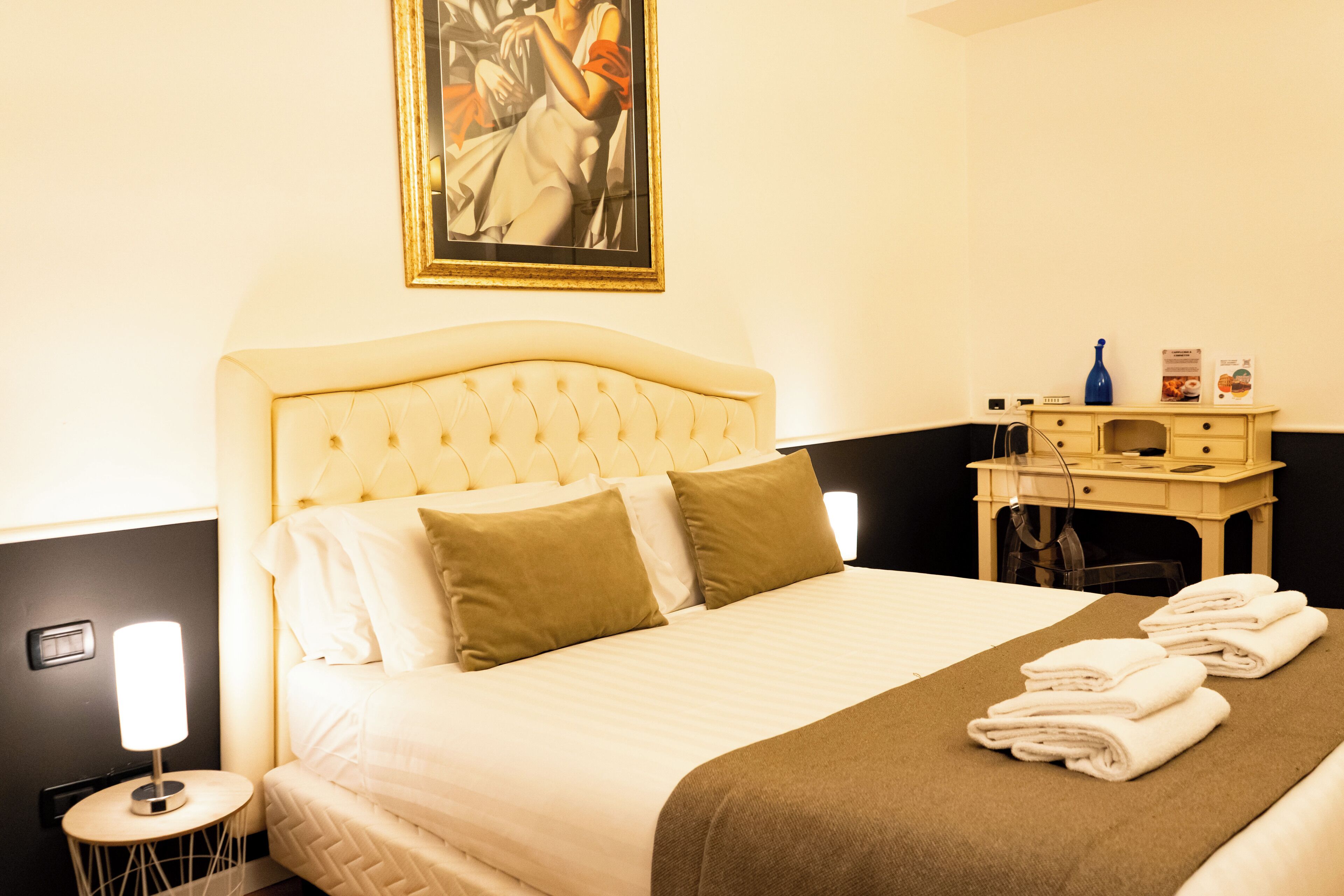 Una camera d'albergo con un letto, un comodino, una lampada e un quadro appeso al muro.