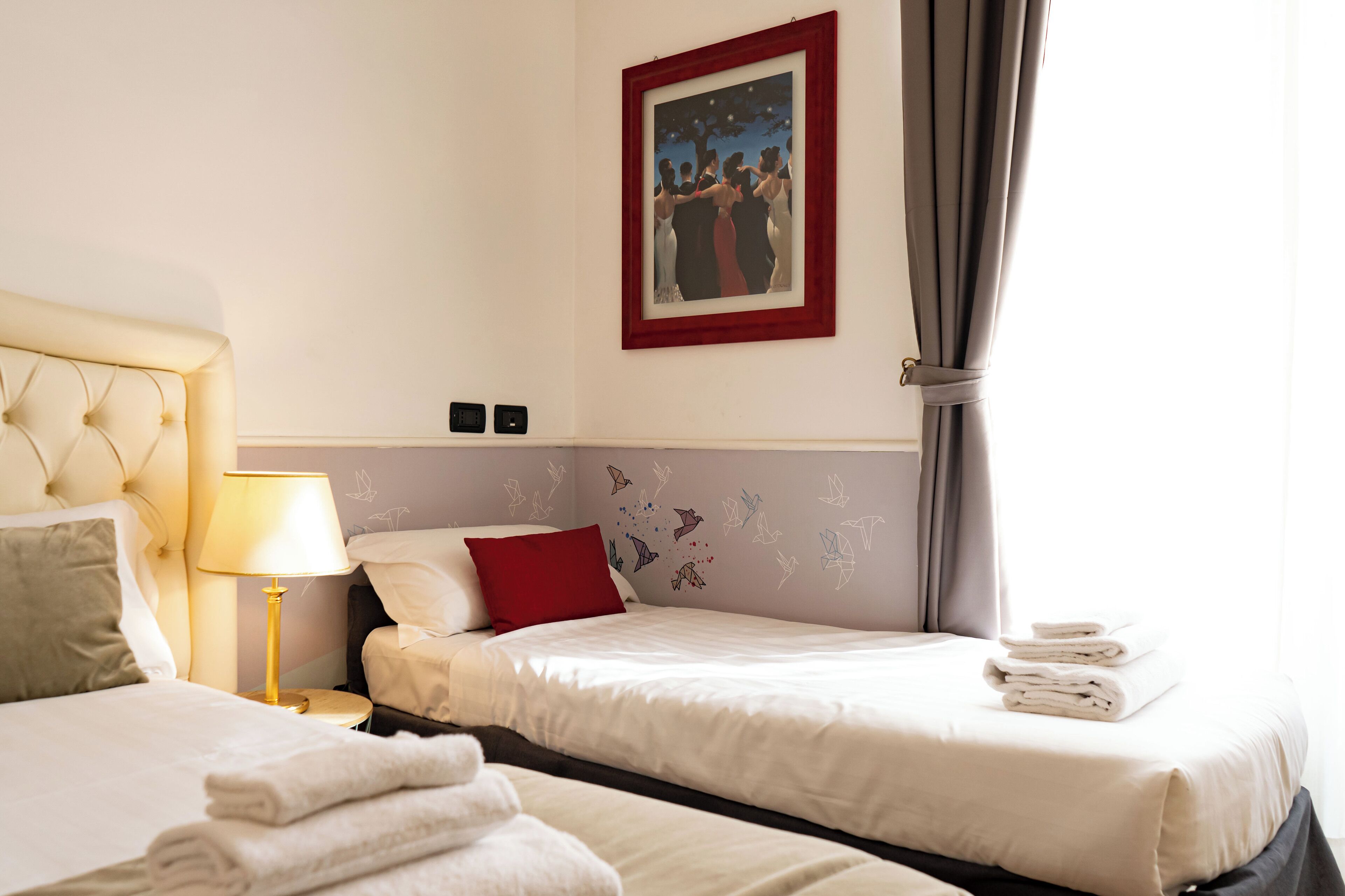 Habitación de hotel con dos camas, una almohada roja, un cuadro colgado en la pared y una lámpara.