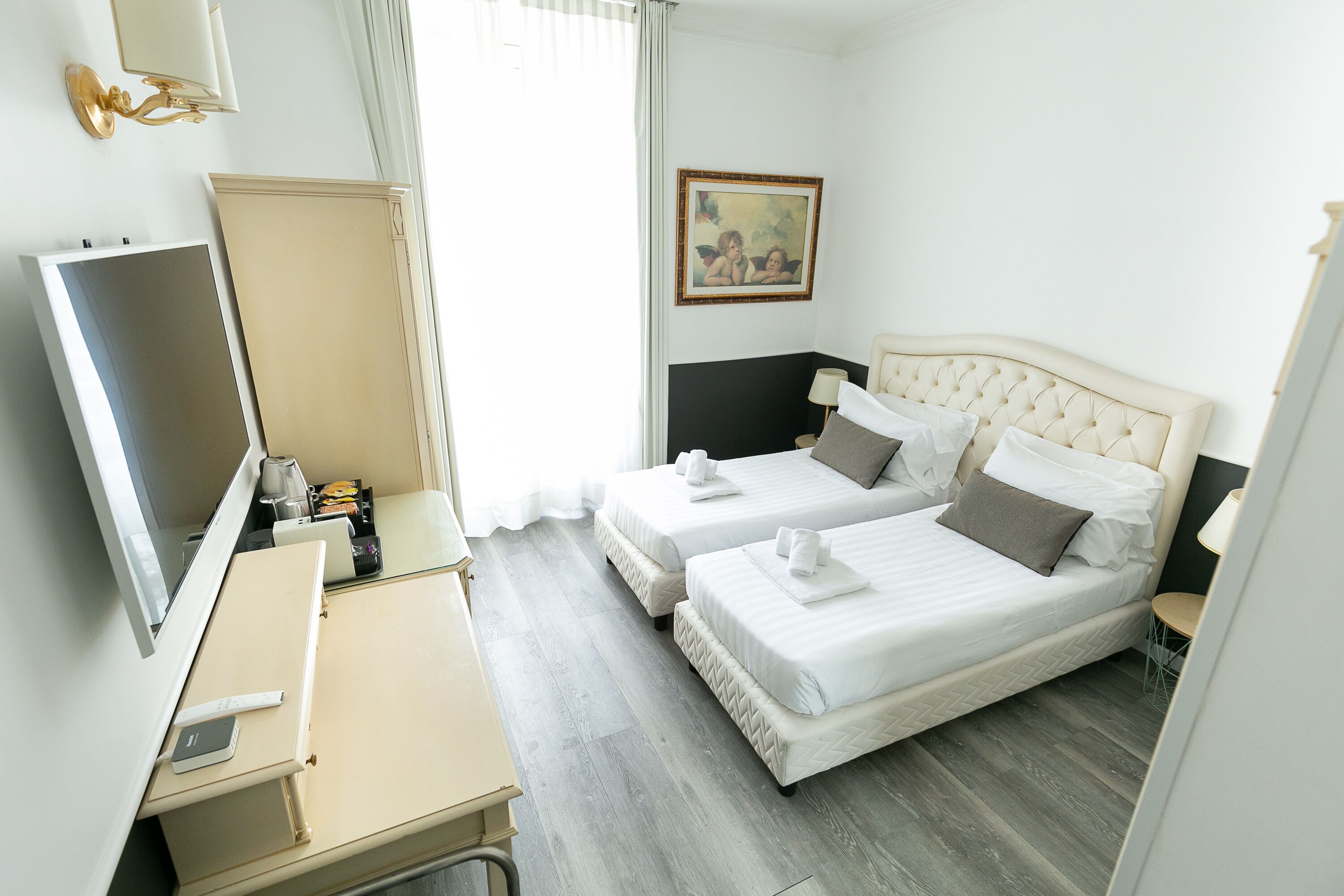 Une chambre d’hôtel avec deux lits, un bureau doté d’un téléviseur à écran plat, un tableau au mur et une fenêtre avec des rideaux.