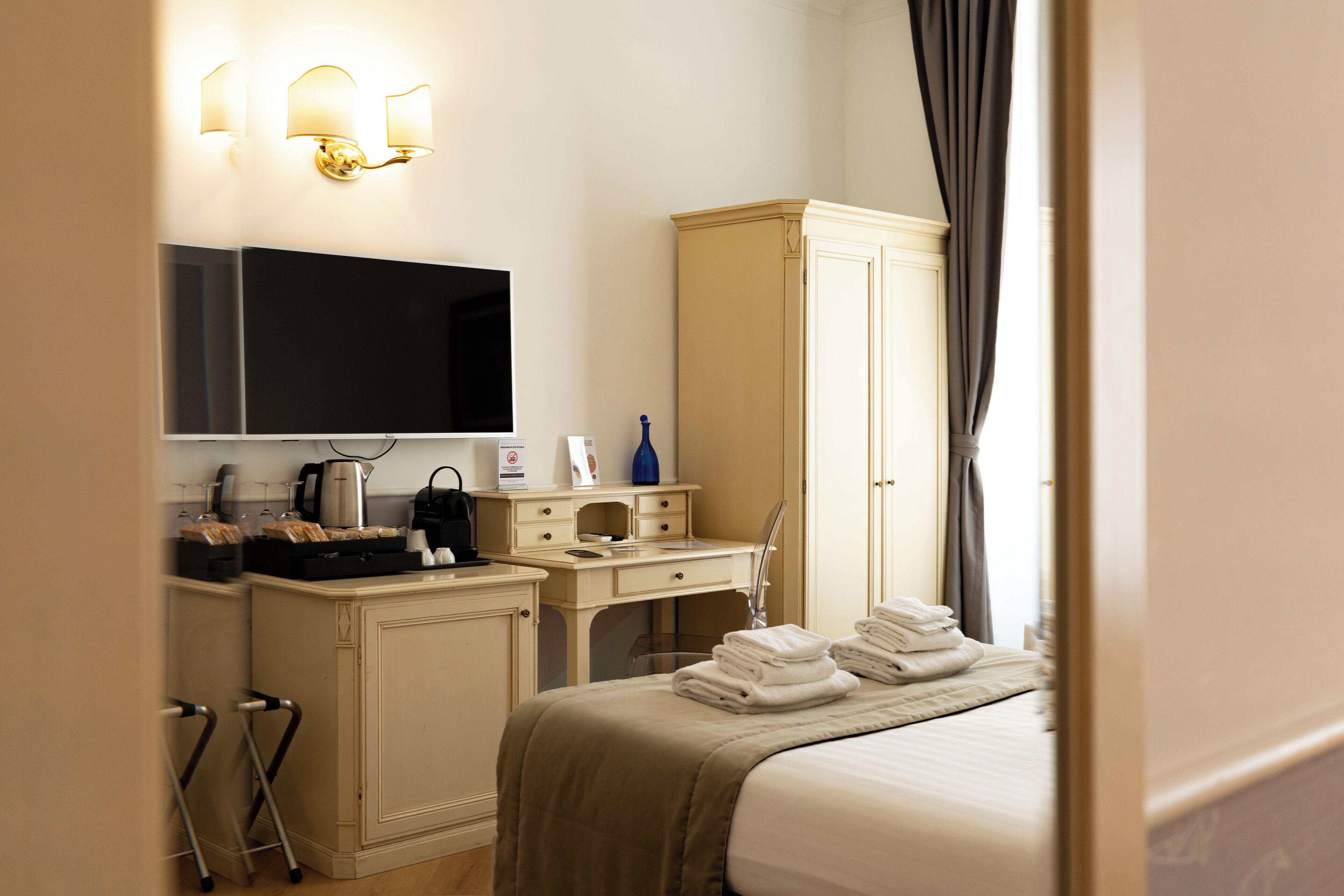 A hotel room with a bed, a desk with a flat-screen TV, a wardrobe, and a bathroom area.
