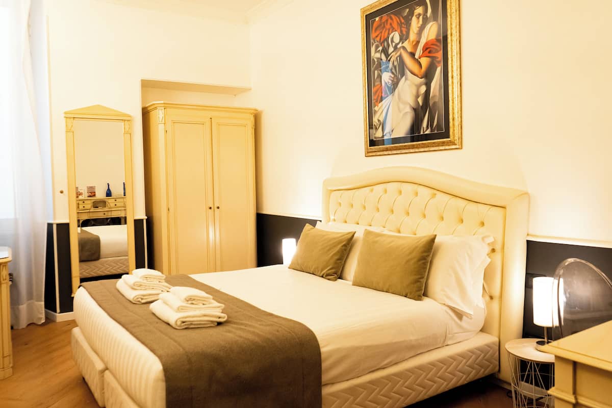 A hotel room with a bed, a wardrobe, a painting, and a nightstand.