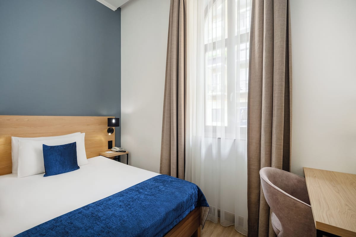 A hotel room with a bed, a desk, and curtains.