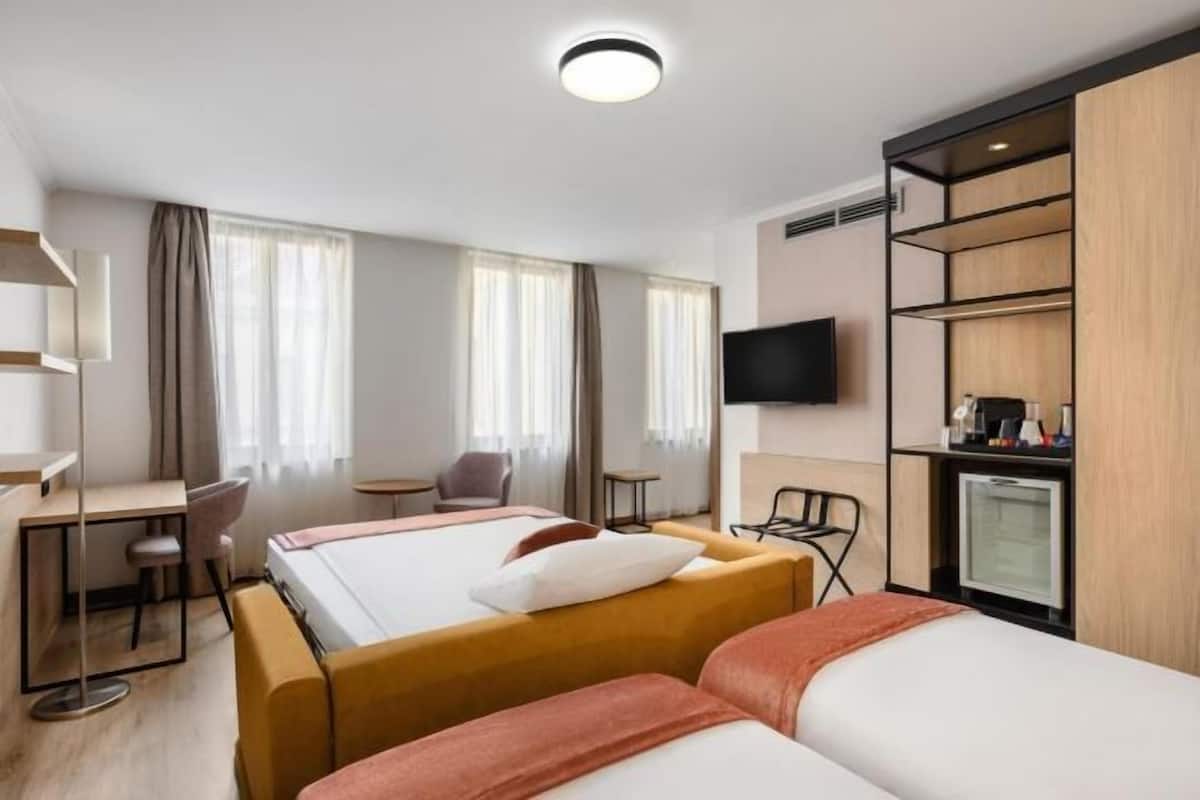 A hotel room with two beds, a desk, a chair, a TV, and a minibar.