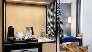 A hotel room with a minibar, a coffee maker, a bottle of water, a small plant, and a mirror reflecting a bed and a chair. - Hotel Bristol Budapest (Budapest)