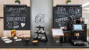 A breakfast bar with a chalkboard sign, a coffee machine, and a bowl of fruit. - Hotel Bristol Budapest (Budapest)