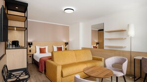 A modern hotel room with a sofa, a small round table, a chair, a bed with pillows, a nightstand, a lamp, and a mirror. - Hotel Bristol Budapest (Budapest)