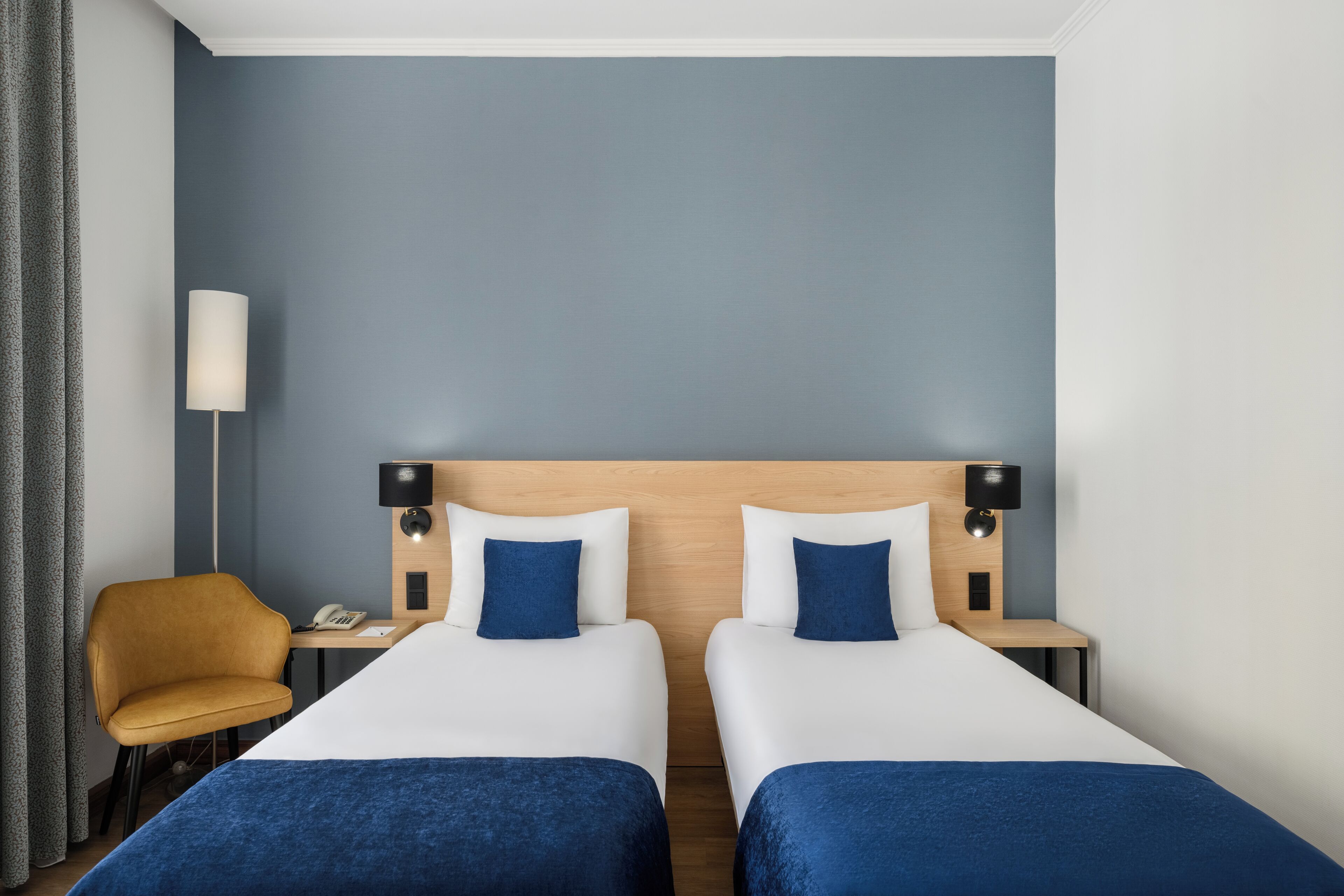 Una habitación de hotel con dos camas, un escritorio, una silla y una lámpara.
