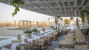 Een terras met tafels en stoelen, met uitzicht op een jachthaven met boten.