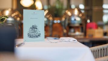 A menu on a table with a candle and a plant in the background.