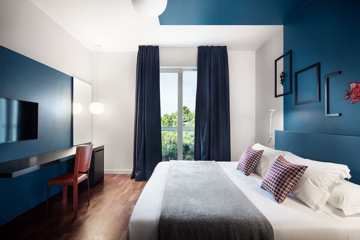 A modern hotel room with a large bed, a desk, and a TV.