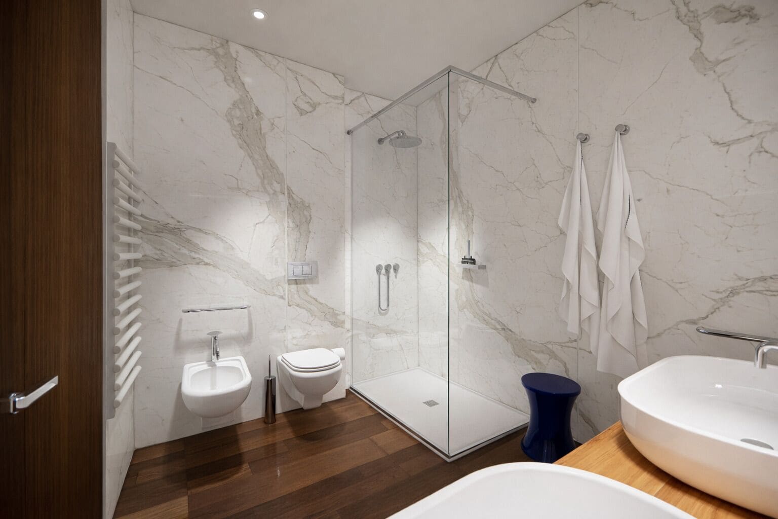 A modern bathroom with a glass-enclosed shower, a toilet, and two sinks.