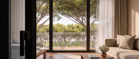 A modern living room with a large sliding glass door leading to a balcony with trees.