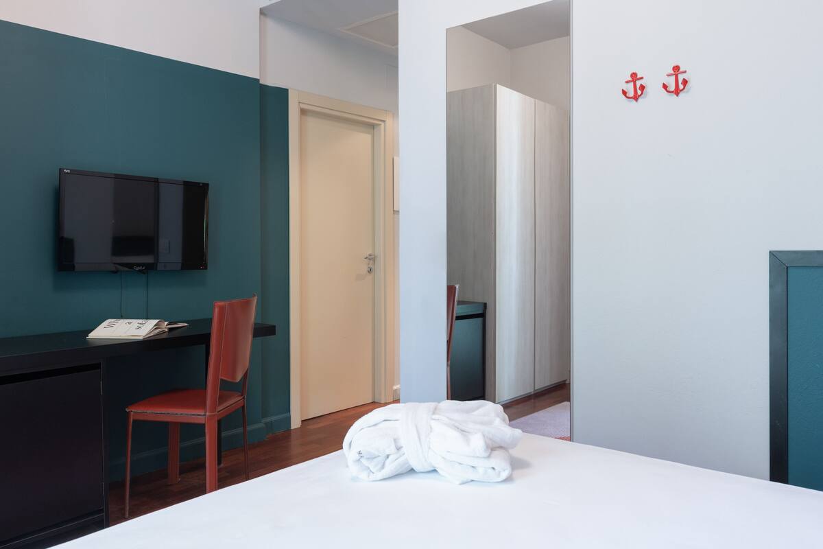 A hotel room with a bed, a desk with a chair, a television, and a door leading to another room.