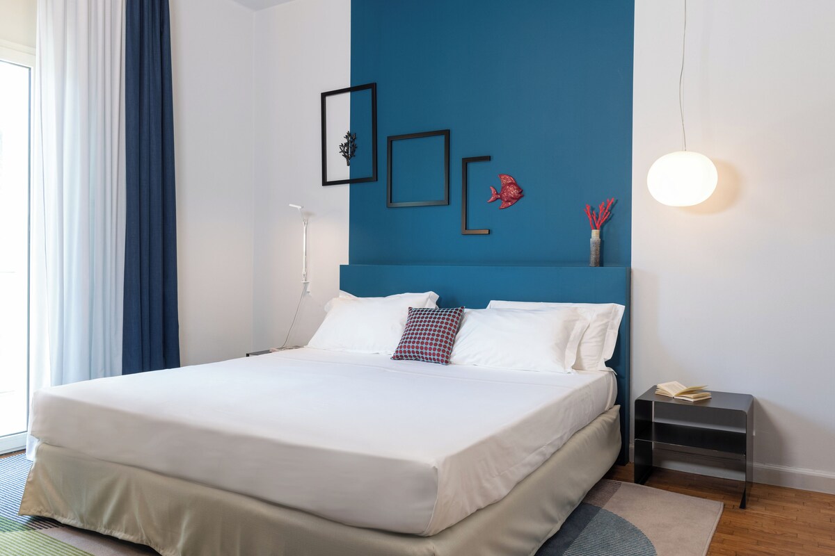 A modern bedroom with a large bed, a bedside table, and a wall-mounted light fixture.
