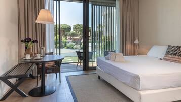 A modern hotel room with a large bed, a dining table, and a view of the outdoors.