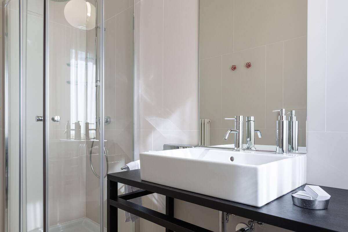 A modern bathroom with a large white sink, a glass shower enclosure, and a black countertop.