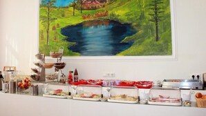 Ein Frühstücksbuffet mit verschiedenen Speisen und einem Landschaftsbild mit See und Bäumen.