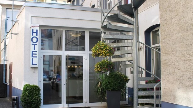 Ein Hotel mit Eingang, Glasdoor, Treppe und einer hängenden Blumenampel.