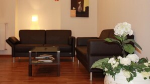 Ein modernes Wohnzimmer mit einem schwarzen Ledersofa, einem Glastisch und einer weißen Vase mit Blumen.