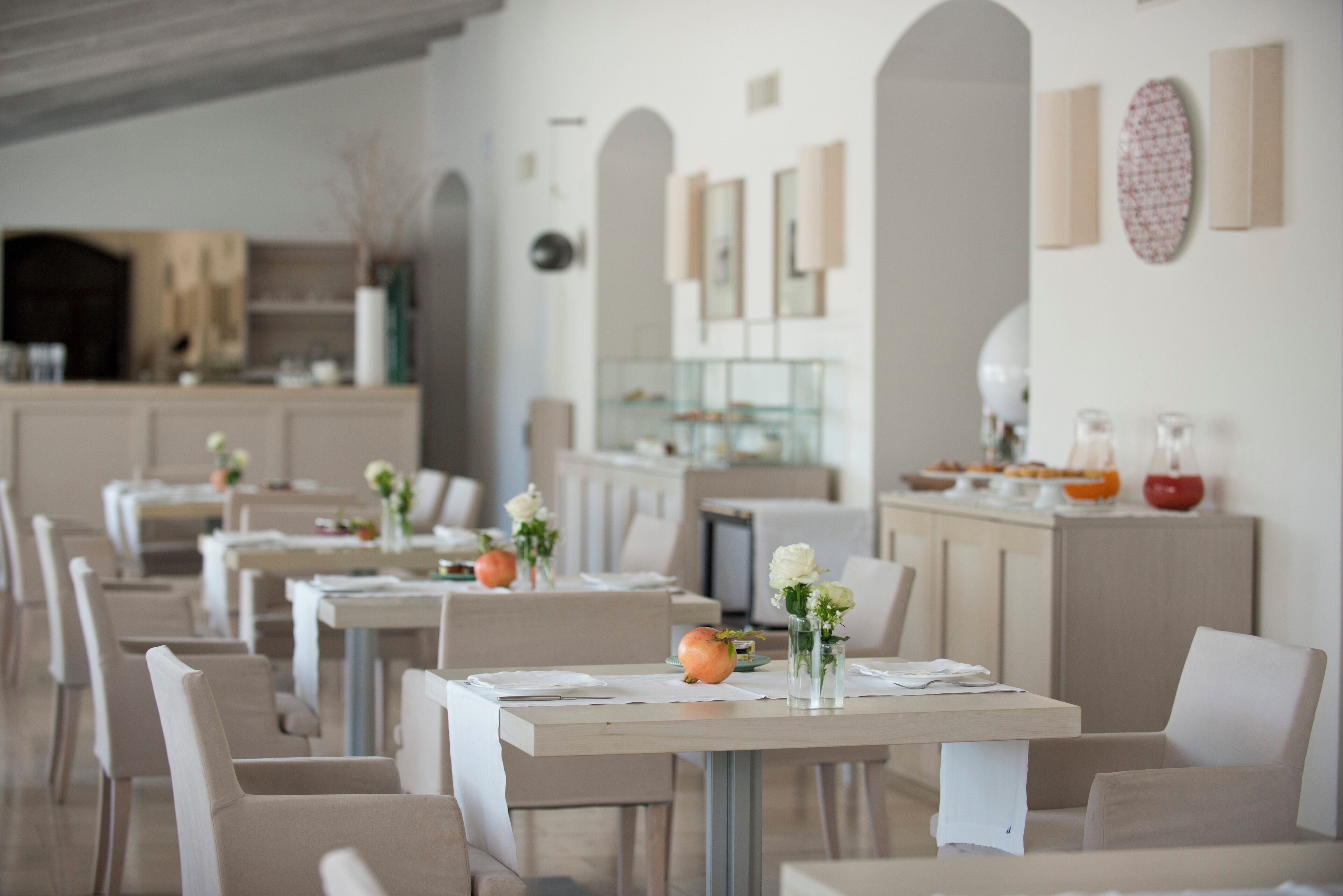 A restaurant with multiple tables, each set with white tablecloths, chairs, and small vases with flowers.