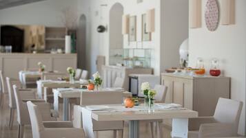 Un restaurante con varias mesas, cada una con mantel blanco, sillas y pequeños jarrones con flores.