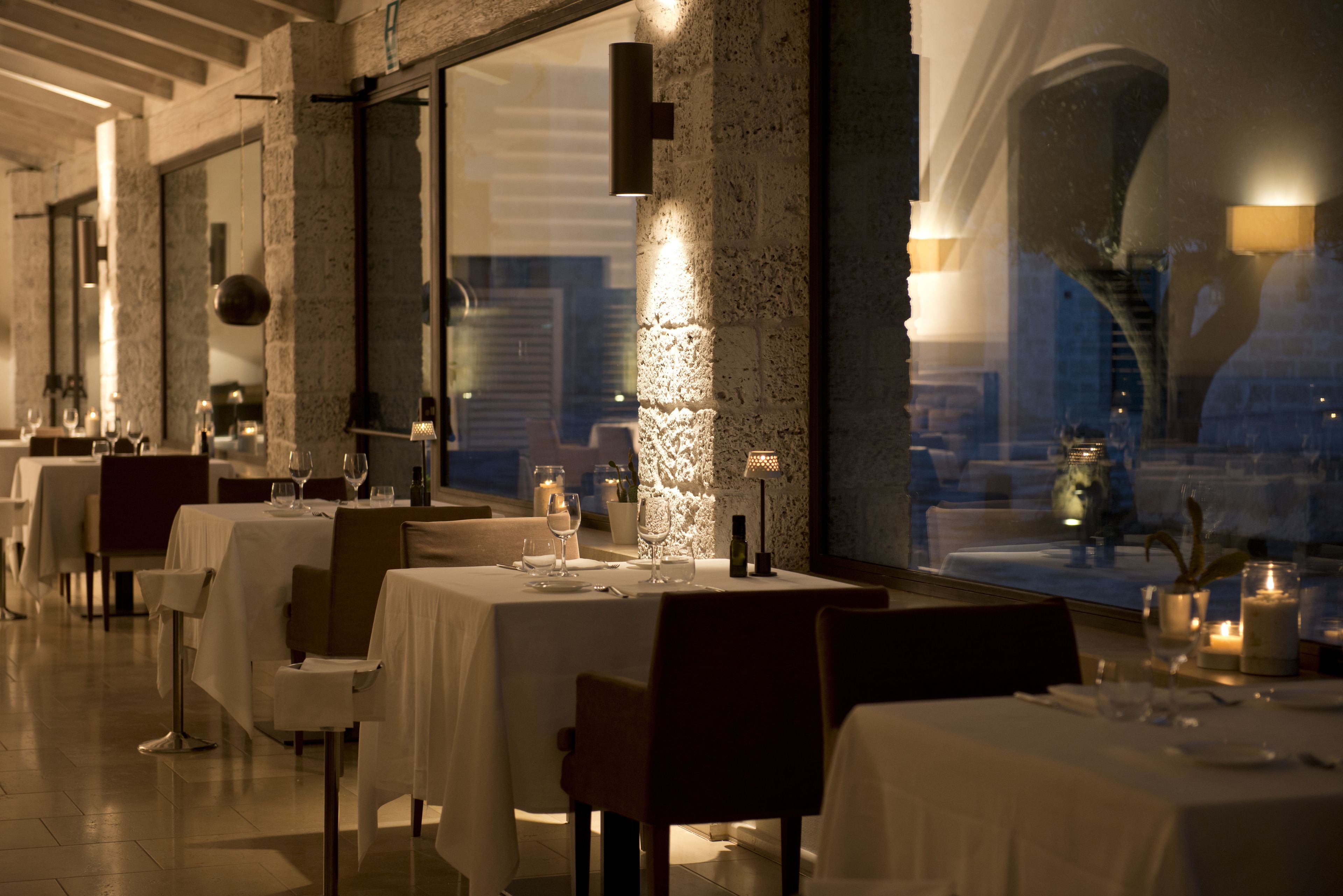 A restaurant with tables set for dining, a large window, and a stone wall.