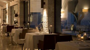 A restaurant with tables set for dining, a large window, and a stone wall.