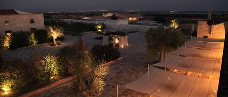 A courtyard with stone pathways, a covered seating area, and illuminated trees.