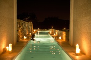 Uma pessoa em um estreito canal de água iluminado, com velas aos lados, sugerindo uma área de spa ou relaxamento.