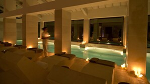 A serene indoor pool area with lounge chairs and candles, suggesting a relaxing atmosphere.