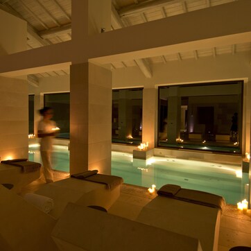 A serene indoor pool area with lounge chairs and candles, suggesting a relaxing atmosphere.