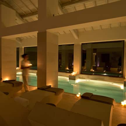 A serene indoor pool area with lounge chairs and candles, suggesting a relaxing atmosphere.