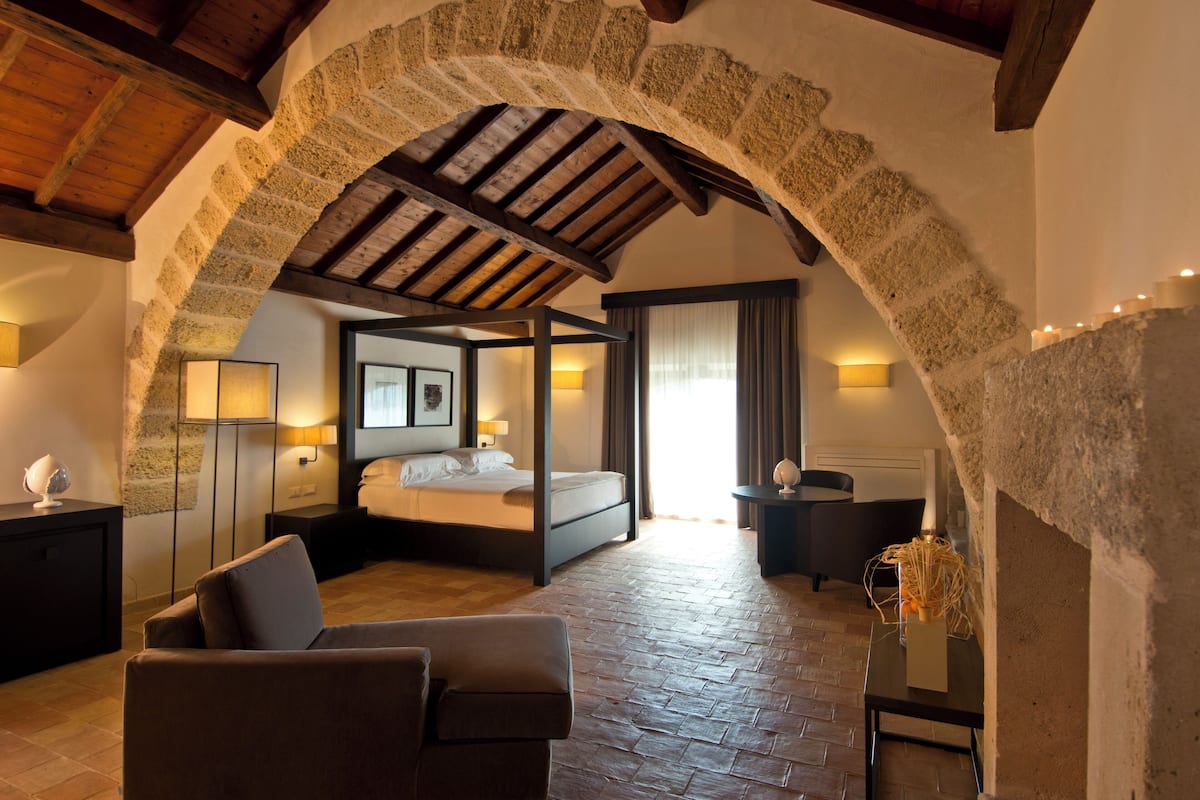 Un dormitorio con cama con dosel, una zona de estar con sofá y un arco de piedra.