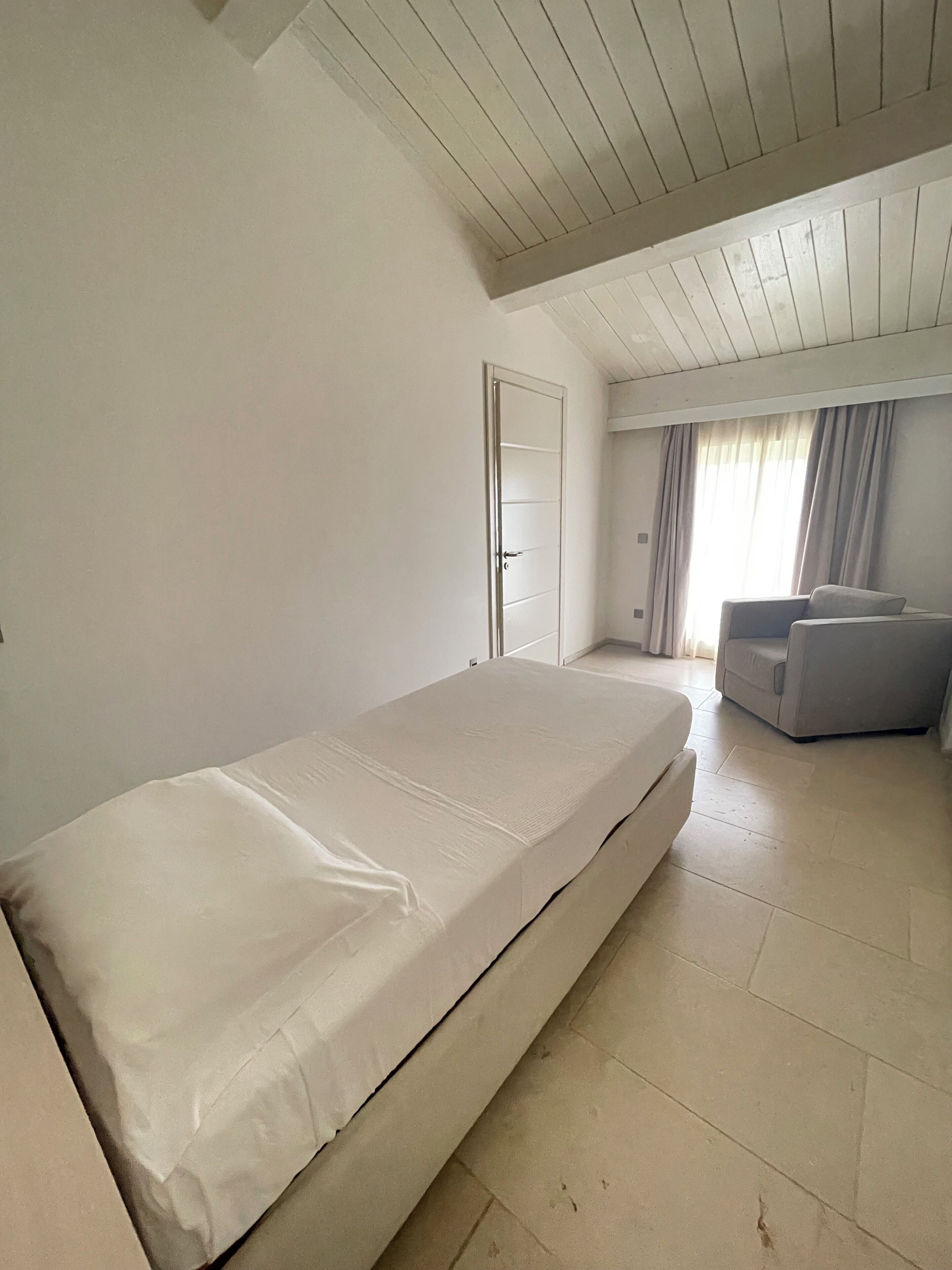 Un dormitorio con cama, puerta, sofá y ventana con cortinas.