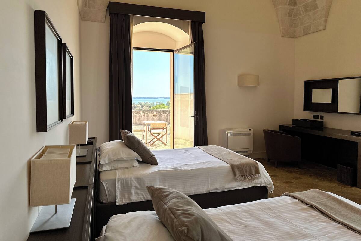 Habitación de hotel con dos camas, un escritorio, una silla, un televisor y un balcón con vistas.