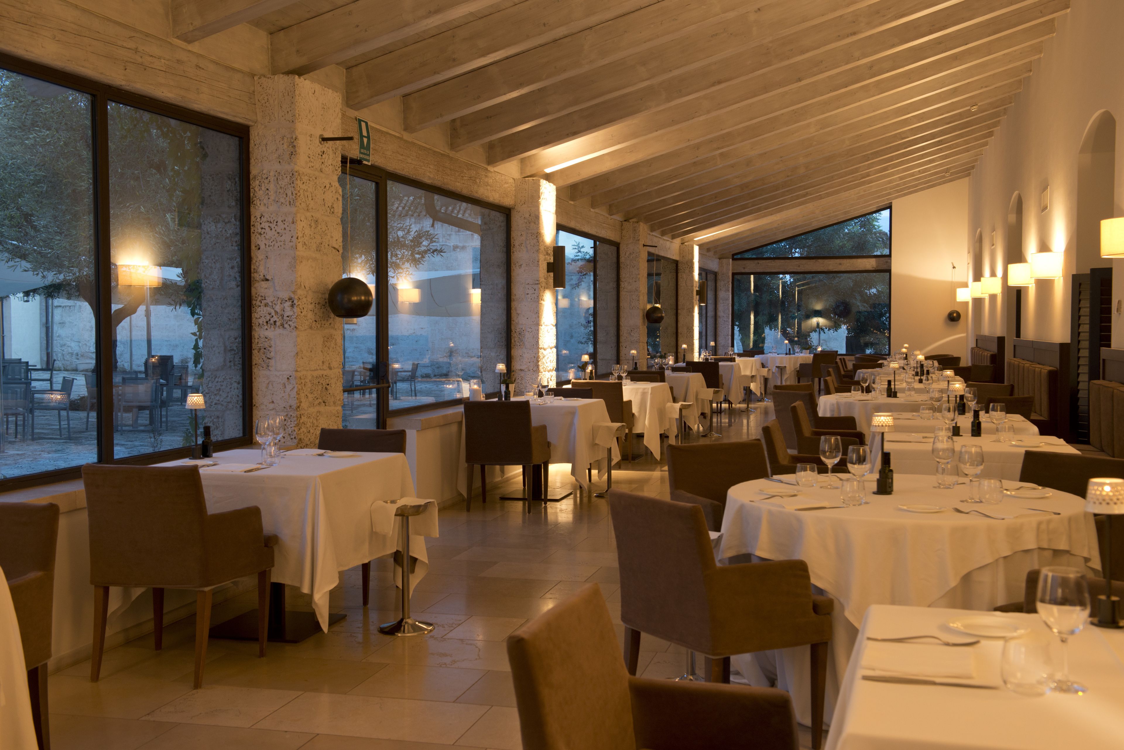 Un restaurante con varias mesas y sillas, ventanas amplias y un techo alto con vigas a la vista.