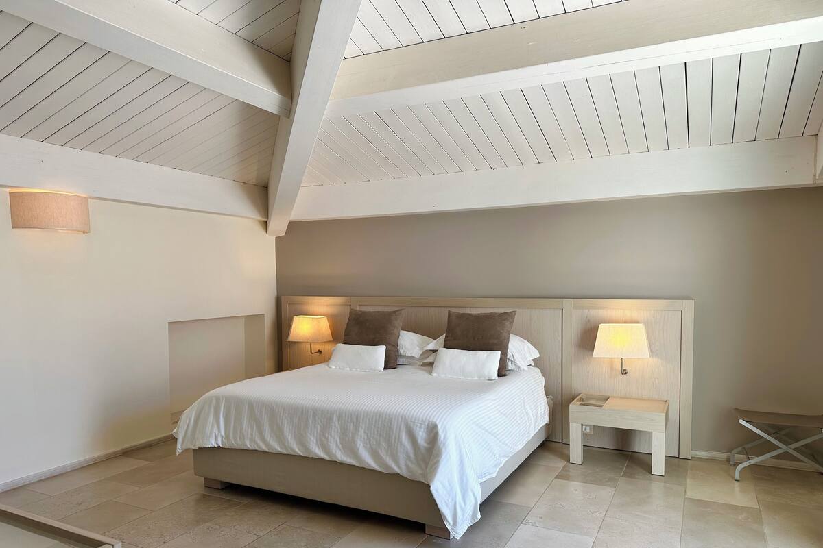 Un dormitorio con una cama grande, dos mesitas de noche con lámparas y una estructura de techo de madera.