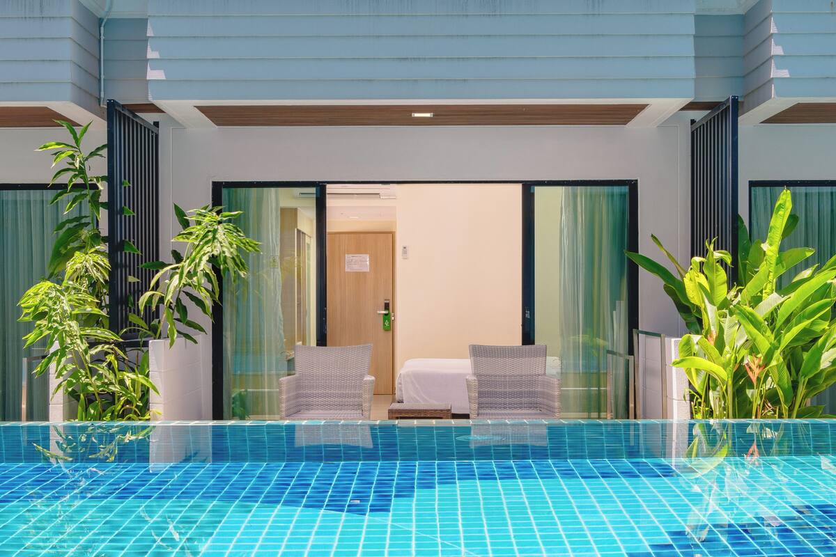 Habitación de hotel moderna con piscina privada, dos sillas de mimbre y una cama.