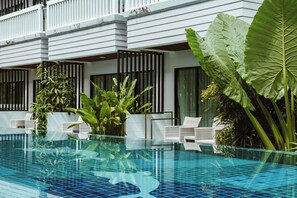 Un hotel moderno con piscina, paredes blancas y plantas verdes grandes.