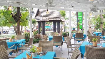 Un restaurante al aire libre con manteles azules, sillas de mimbre y un pabellón.