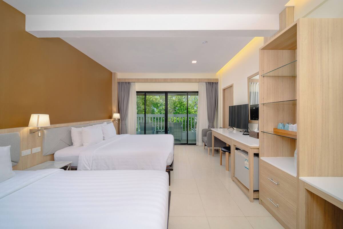 Habitación de hotel con dos camas, un escritorio, un televisor y un balcón con cortinas.