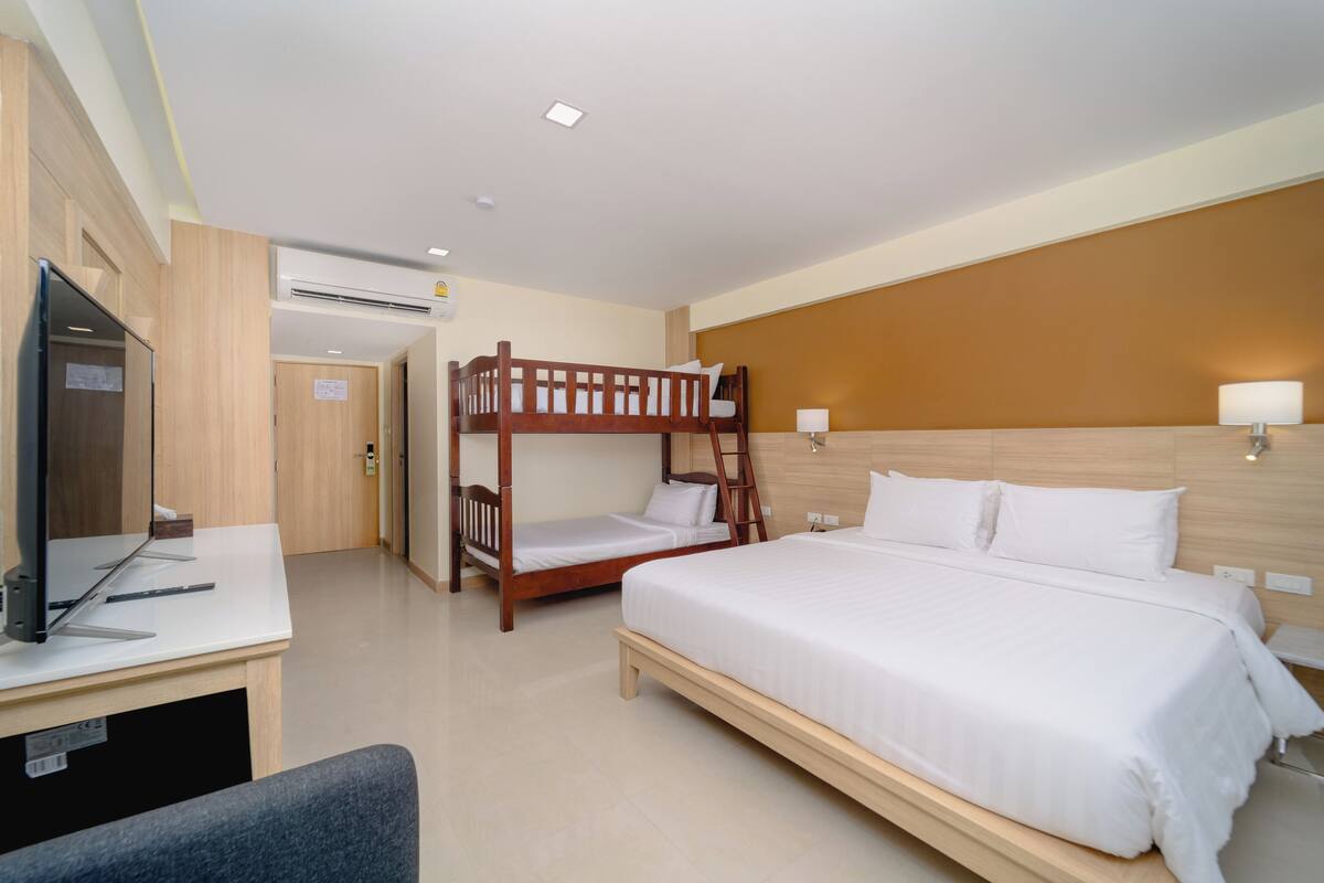 Habitación de hotel con una cama individual, una litera, un escritorio con computadora y televisión.