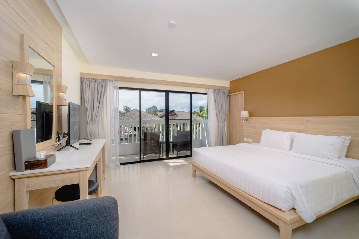 Habitación de hotel con cama, escritorio, televisión y balcón con vistas a las montañas.