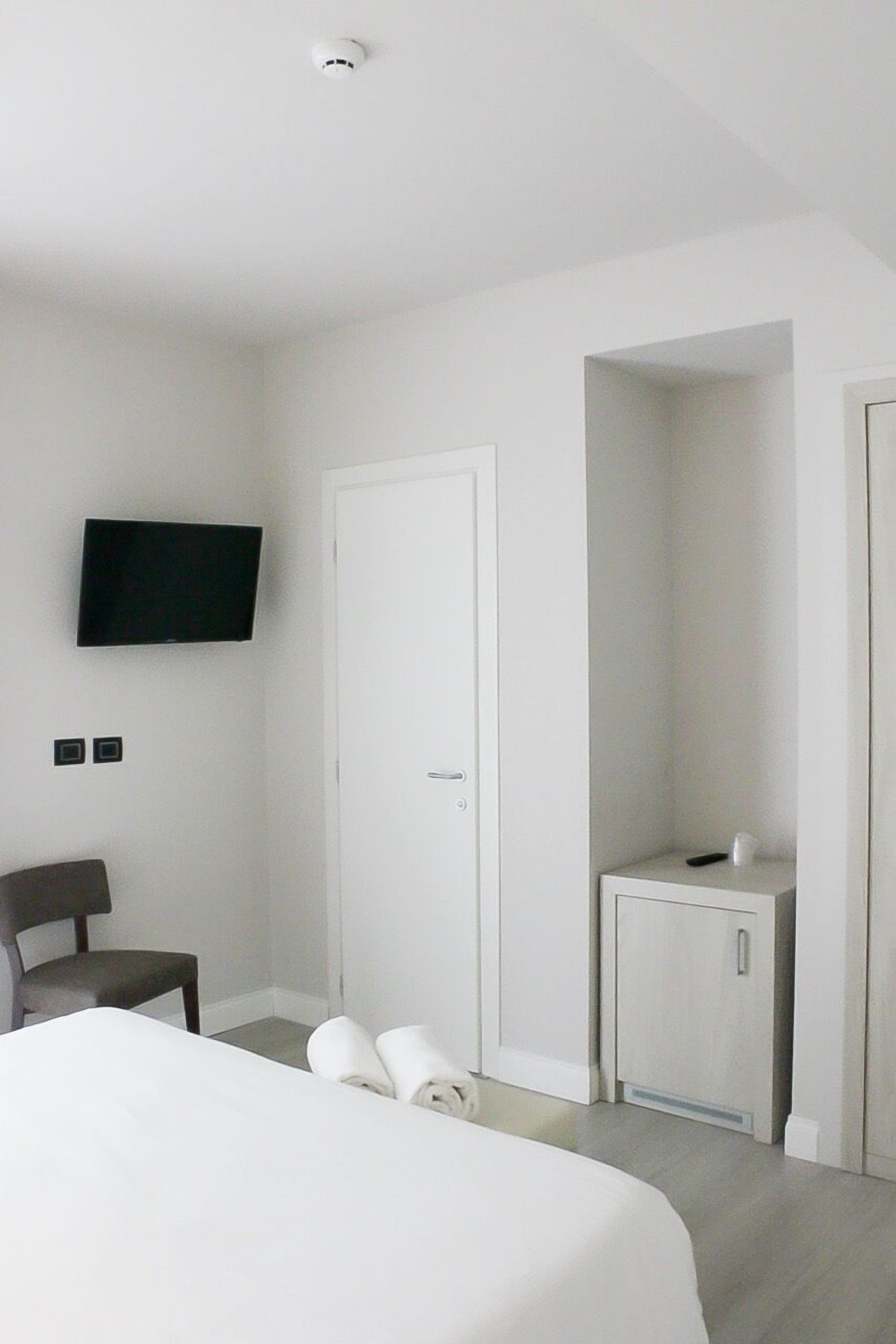 Een hotelkamer met een bed, een aan de muur bevestigde televisie, een stoel, een klein kastje en een deur.