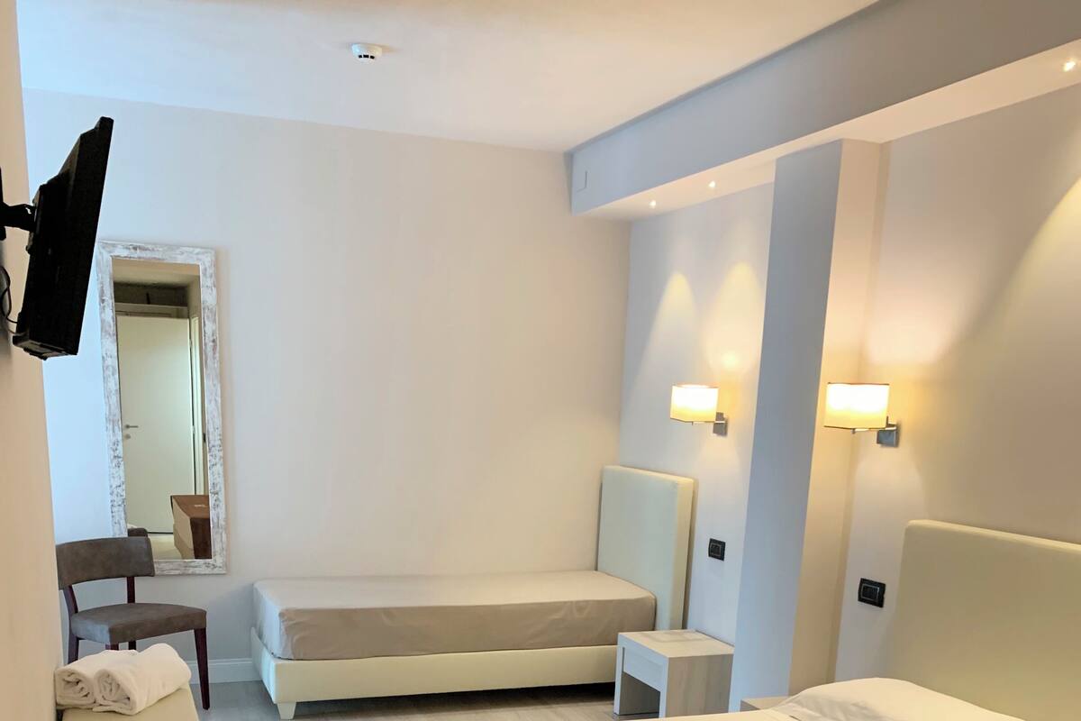 Ein modernes Hotelzimmer mit einem großen Bett, einem Nachttisch, einem Sessel, einem an der Wand befestigten Fernseher und einem Spiegel.
