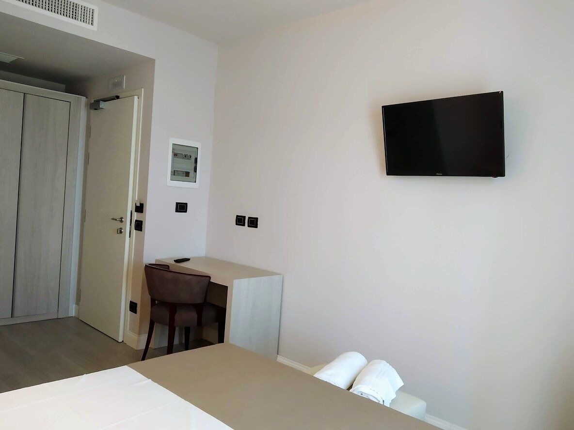 Habitación de hotel con cama, escritorio, silla, televisor montado en la pared y puerta que da a otra habitación.