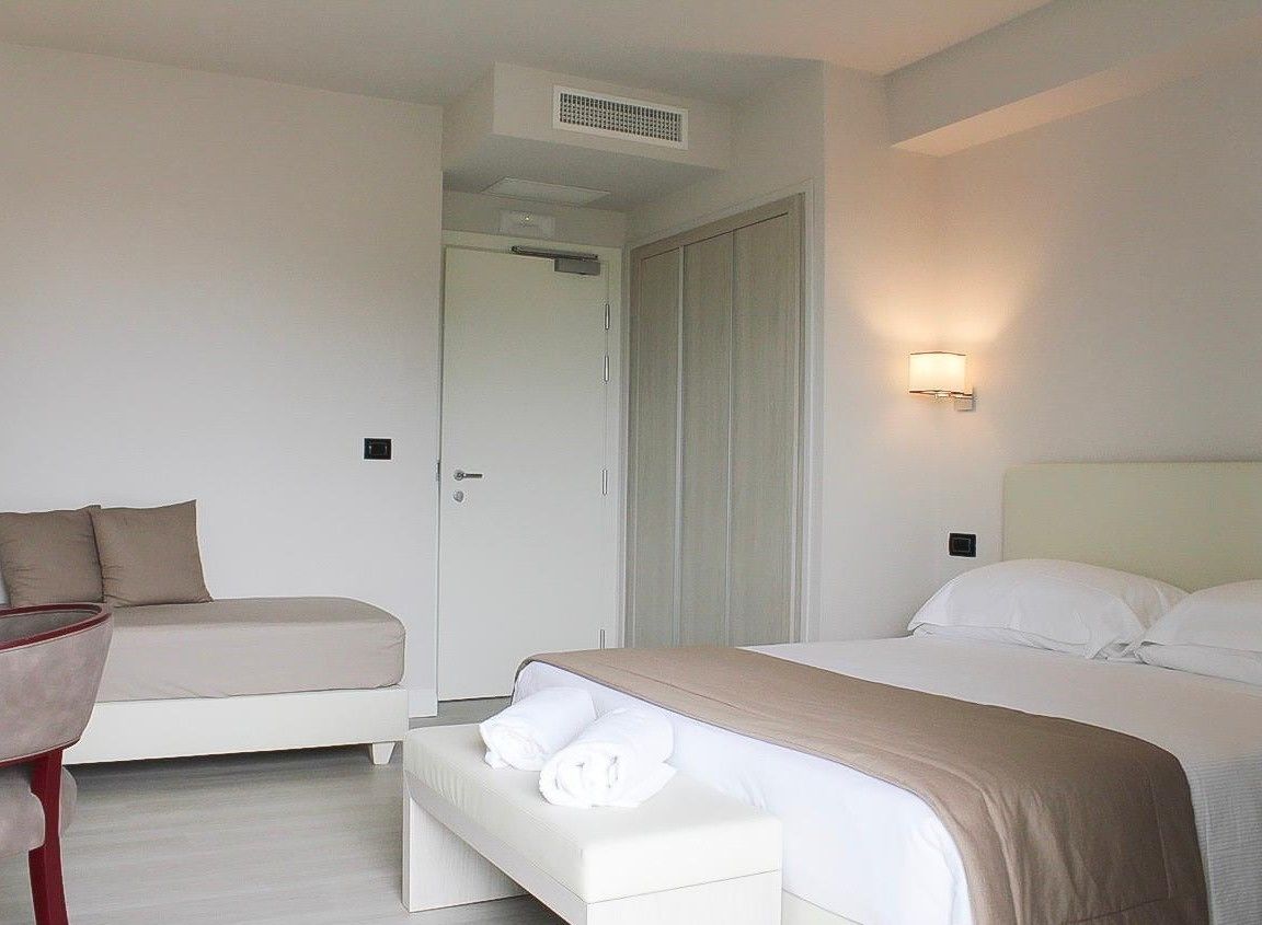 Una habitación de hotel moderna con cama, mesita de noche, sofá y armario.