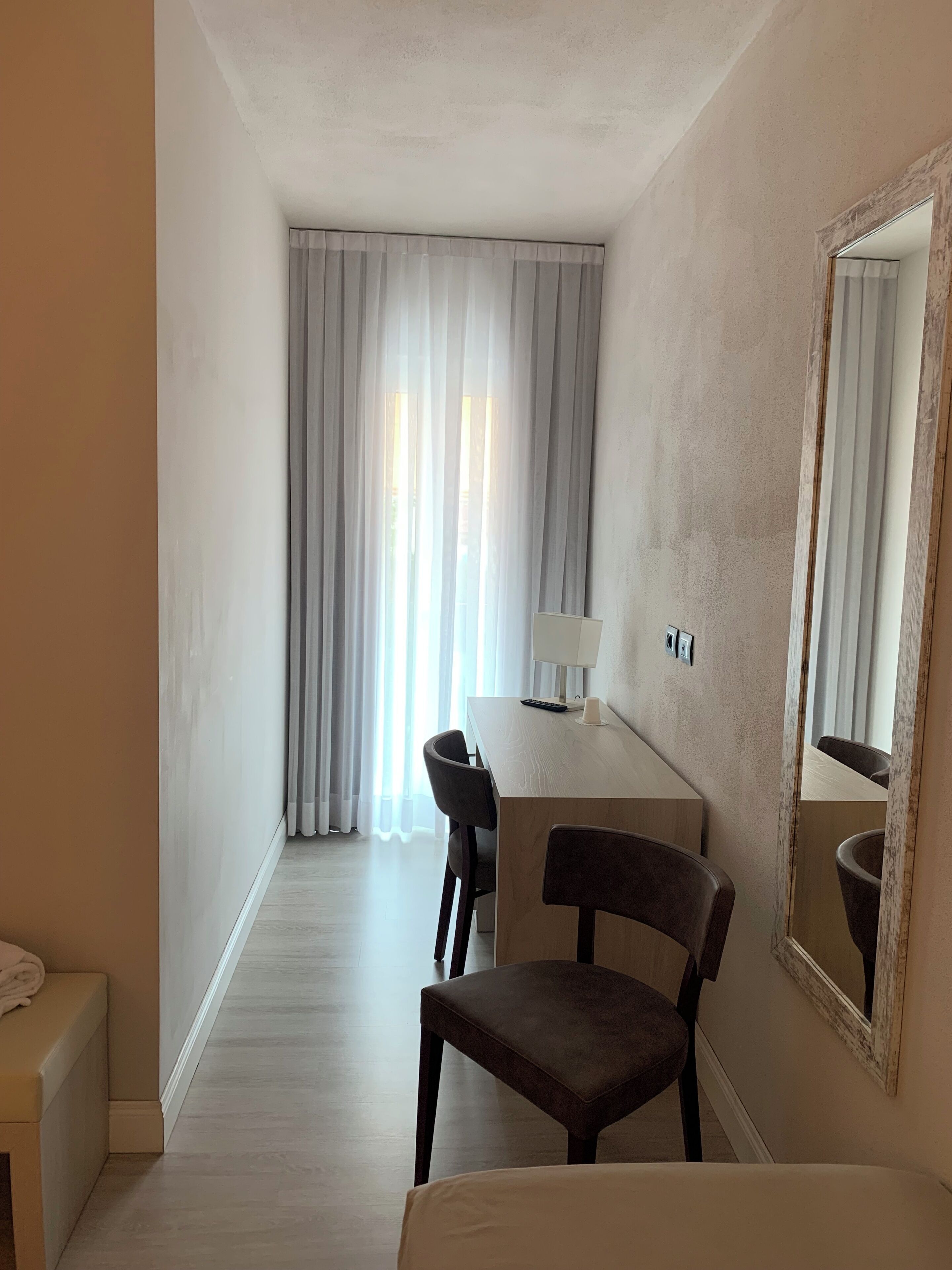 A hotel room with a bed, a desk, a chair, a lamp, and a mirror.