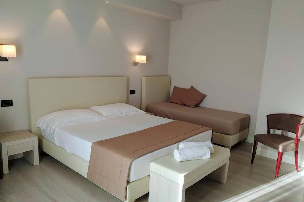 Ein Hotelzimmer mit einem großen Bett, einem Einzelbett, einer Bank, einem Sessel und zwei Nachttischen.